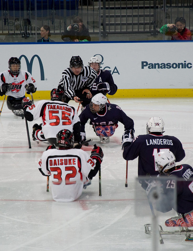 Photo of Ice Sled Hockey team United States (blue shirts) vs Japan (white shirts) during the 2010 Paralympics in Vancouver. Credit: By popejon2 via Wikimedia Commons.